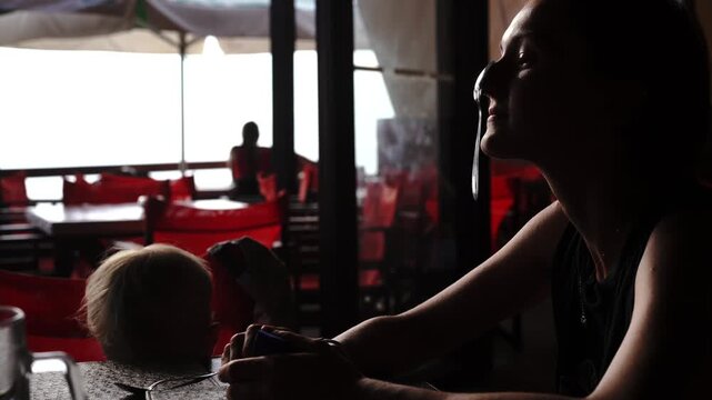  Playful mother and son balance teaspoons on their noses and laugh together while waiting for food at a restaurant.