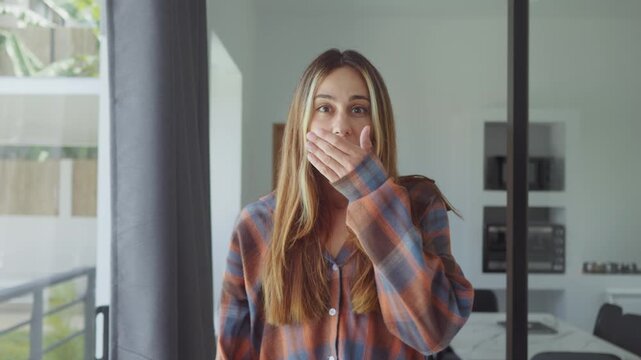 wow reaction woman with glasses in modern home interior expressing surprise and disbelief to camera. wow reaction woman covering mouth and staring at camera feeling shocked and amazed indoors