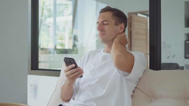 Healthcare concept man suffering from neck pain at home touching sore muscles with discomfort. Healthcare theme showing muscle tension poor posture and need for treatment and therapy
