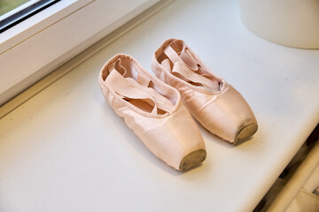 Worn ballet pointe shoes on window sill with soft natural light © TRAVELARIUM