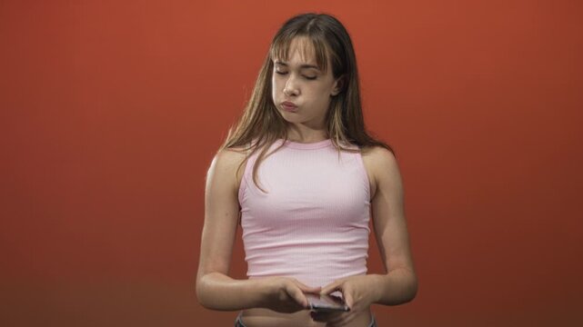 Young woman holding smartphone and tapping screen, exposed midriff with visible navel and eyes rolling in studio; boredom digital life.