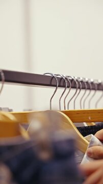 Close-up view of a clothing rack lined with wooden hangers and denim garments, with a shopper's hand browsing the neatly arranged apparel in a minimalist retail boutique interior