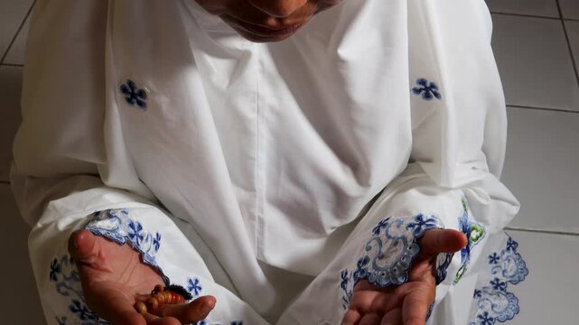 a Muslim woman is praying using a mukena and prayer beads
