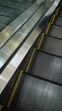 Close-up of moving escalator steps with yellow safety lines, reflective metal side panel, and lit warning indicator, capturing transit architecture with industrial detail