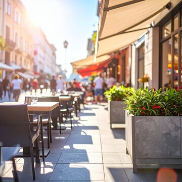 Empty tables at an outdoor cafe on a sunny street with blurred people walking by.