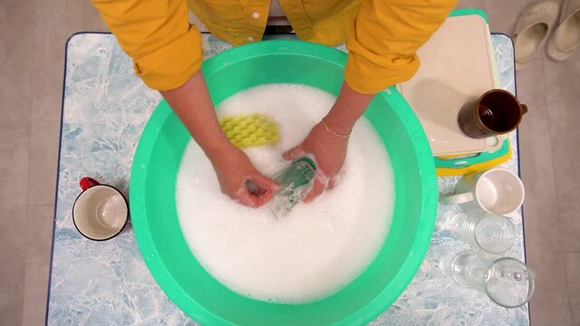 Washing dishes in a turquoise basin with soap bubbles on a kitchen countertop in a bright, cheerful setting