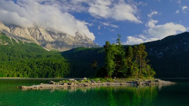 Static shot of a small island in Eibsee lake reflecting the Zugspitze mountains and blue sky in the Bavarian Alps, Germany.