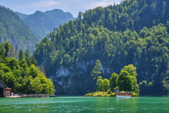 A white electric passenger boat glides past the small Christlieger island on the turquoise Konigsee lake in Berchtesgaden National Park, Bavaria, Germany.