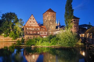 Fototapeta premium Night view of the illuminated Weinstadel and medieval towers reflecting in the Pegnitz river in Nuremberg, Bavaria, Germany.