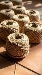 Obraz premium Close-up of numerous natural jute twine spools arranged on a terracotta surface, bathed in warm sunlight, highlighting their rustic texture and earthy tones.