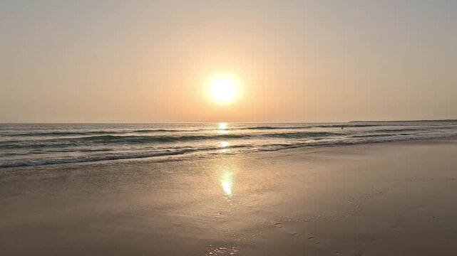 Handheld beautiful video of the sunset or sunrise over the horizon of gentle ocean waves, with clear sky at golden hour, seen from the beach creating a peaceful and serene seascape