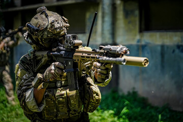 Fototapeta premium Soldier in camouflage gear aims tactical rifle with advanced optics and suppressor