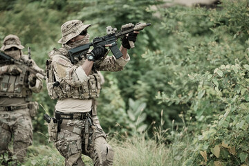 Obraz premium Two soldiers in camouflage gear aiming rifles in a dense green forest environment