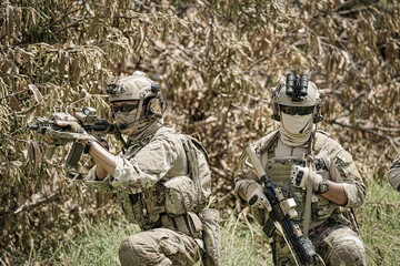 Fototapeta premium Two soldiers in camouflage gear aiming rifles in a dense forest environment