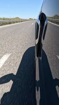 Vertical view from a low angle of the side of a vehicle traveling on a highway, on a sunny day with a clear blue sky, with reflections on the car
