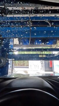 Vertical video of POV inside a car wash tunnel during the drying process, with air blowers and water droplets on the windshield creating a dynamic interior view