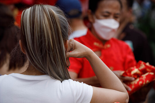 Female tourist standing with hand on chin, Thai weekend market lifestyle, unposed movement, natural candid motion, rear view.