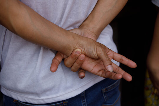 Man's hands clasped behind back while standing, unposed movement, natural candid motion, showing skin texture and nails, close up.