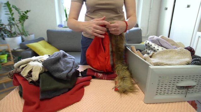 Person organizing colorful clothing and accessories on a table in a cozy indoor space during daylight