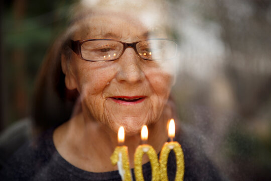 Portrait of an elderly woman with glasses holding anniversary candles.  An old woman holds a birthday cake alone on her centenary.