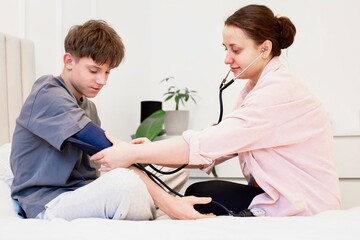 Obraz premium Teen boy having blood pressure measured at home by mother or doctor, heart health and prevention