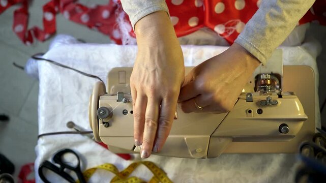 A person skillfully operates a sewing machine, focusing on adjusting the thread tension while surrounded by vibrant fabric scraps, scissors, and measuring tape in a creative workspace.