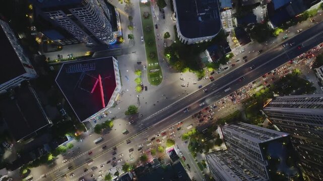 Top-down drone capture of Hanoi urban intersection with heavy traffic, light trails, and modern buildings forming a vibrant nighttime cityscape along Minh Khai Street.