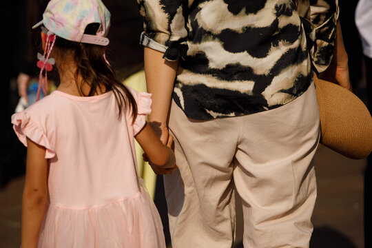 Mother holding daughter's hand walking in Thai temple, travelers discovering Thai cultural heritage, unposed movement, rear view, at Wat Pho.