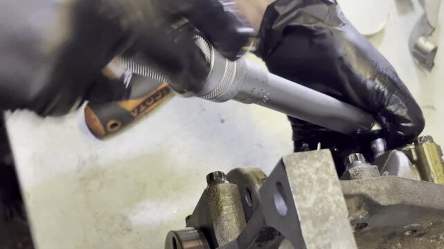 Mechanic using torque wrench on engine part with black gloves.