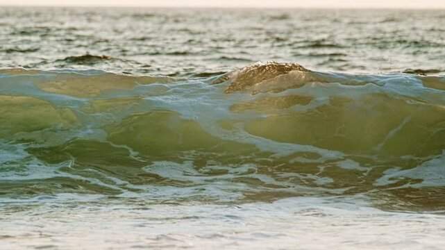 The ocean wave breaks under the setting sun in Fonte da Telha, Costa da Caparica, Portugal. This slow motion capture shows the beauty of water and nature during sunset.