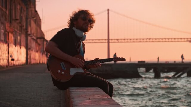 Hipster street musician in black playing electric guitar in the street on sunset
