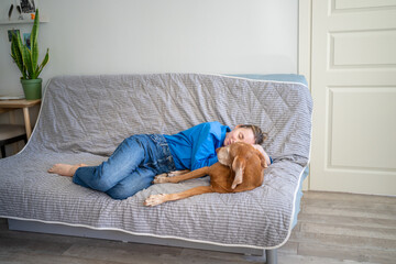 Relaxed woman gently hugging dog on couch, sharing warm affection, bonding at home. Unconditional...