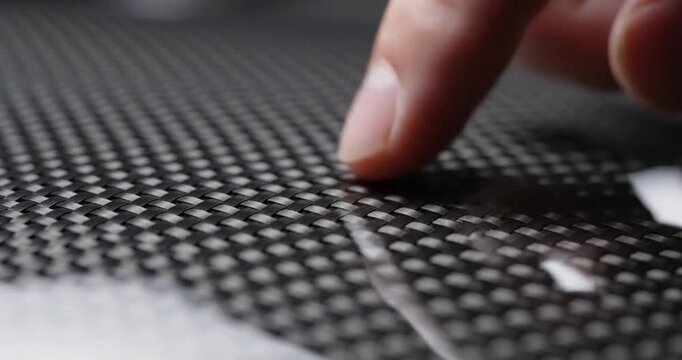 Close-up of a finger gently touching a textured carbon fiber surface, highlighting tactile interaction