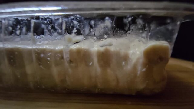 Sesame halva in a transparent plastic container. Close-up side view of traditional Mediterranean sweet in retail packaging on a wooden surface.