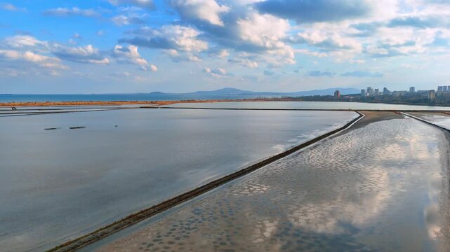 Wide panoramic view of salt pans and sea horizon. High angle view of large salt evaporation fields separated by dikes leading to the sea.