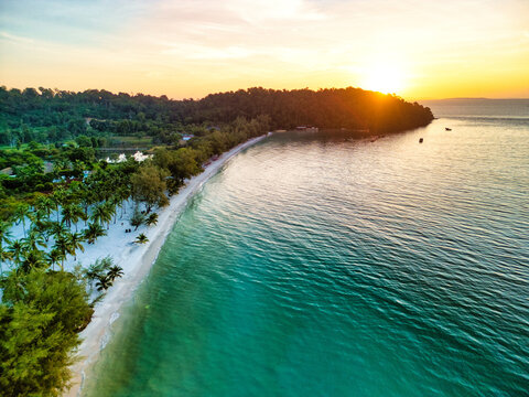 Aerial view of the soft white sands kissed by the turquoise sea, where the lush green forest meets the horizon at sunset, Preah Sihanouk, Sihanoukville, Cambodia.