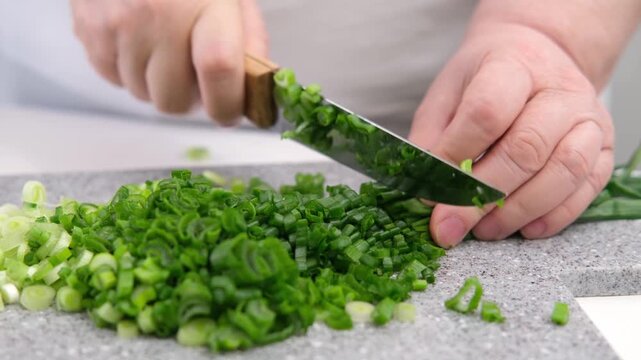 Female hands cutting green onions on a grey board