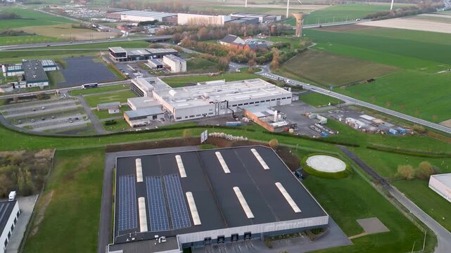 Aerial view of industrial buildings and green fields, a water tower, and wind turbines create a contrasting landscape, Ath, Wallonia, Belgium.