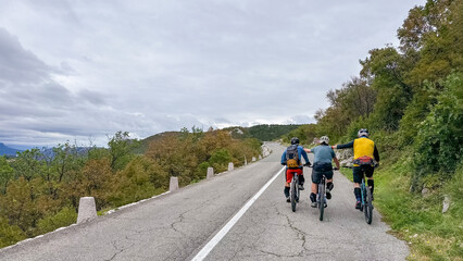 Obraz premium Three friends cycling together on a mountain road surrounded by trees and overcast sky