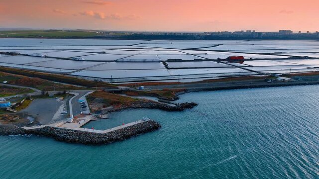 Aerial perspective of coastal salt ponds and harbor pier. View of salt production basins and a stone pier at the sea shore.