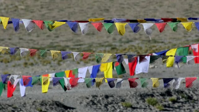 A cinematic close-up of vibrant Buddhist prayer flags fluttering in the wind near Pangong Lake.