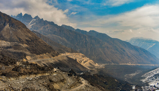 Remote mountain road with rocky snow-dusted Himalayan cliffs under overcast sky in North Sikkim.