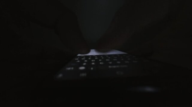 Close-up silhouette of thumbs rapidly navigating a glowing smartphone keyboard in a pitch-black room, highlighting a sense of urgent late-night communication or secret messaging.