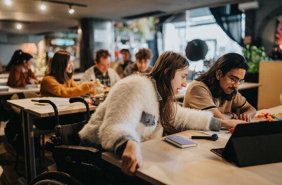 A diverse group of students study together at shared desks, including a student in a wheelchair.