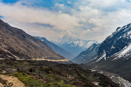 Meandering river through wide Himalayan valley with snow-capped mountains and rugged terrain in North Sikkim landscape.