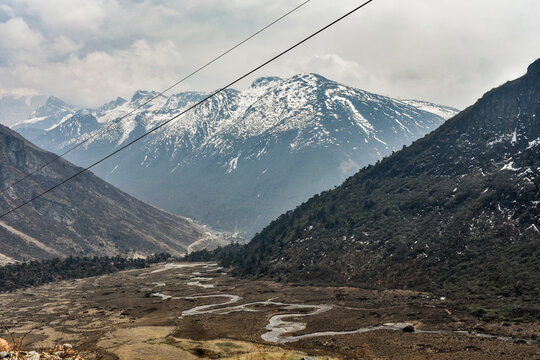 Meandering river through wide Himalayan valley with snow-capped mountains and rugged terrain in North Sikkim landscape.