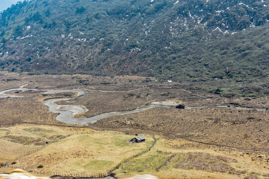 Meandering river through wide Himalayan valley with snow-capped mountains and rugged terrain in North Sikkim landscape.