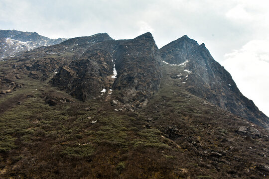 Rugged Himalayan mountain peaks with snow patches under cloudy sky, showcasing dramatic high altitude landscape in North Sikkim.