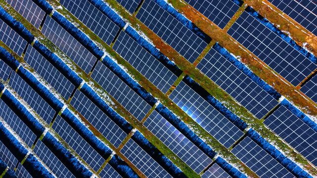 Abstract aerial texture of blue solar panel array. High angle shot of repeating rows of photovoltaic modules on a grassy surface. Clean energy technology.