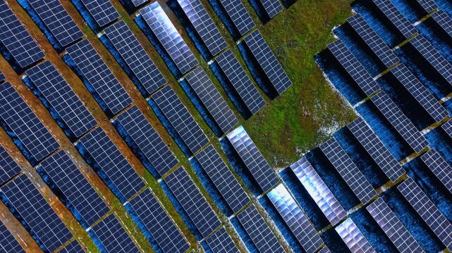 Solar panel arrays with sun reflection from above. Aerial view of solar modules on green grass showing bright sun glints and reflections on some panels.
